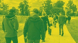 Photograph of a crowd walking through the outside riverfront space at the Fuller Land Lab. 