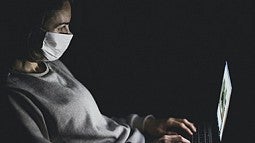 Person wearing mask in front of computer