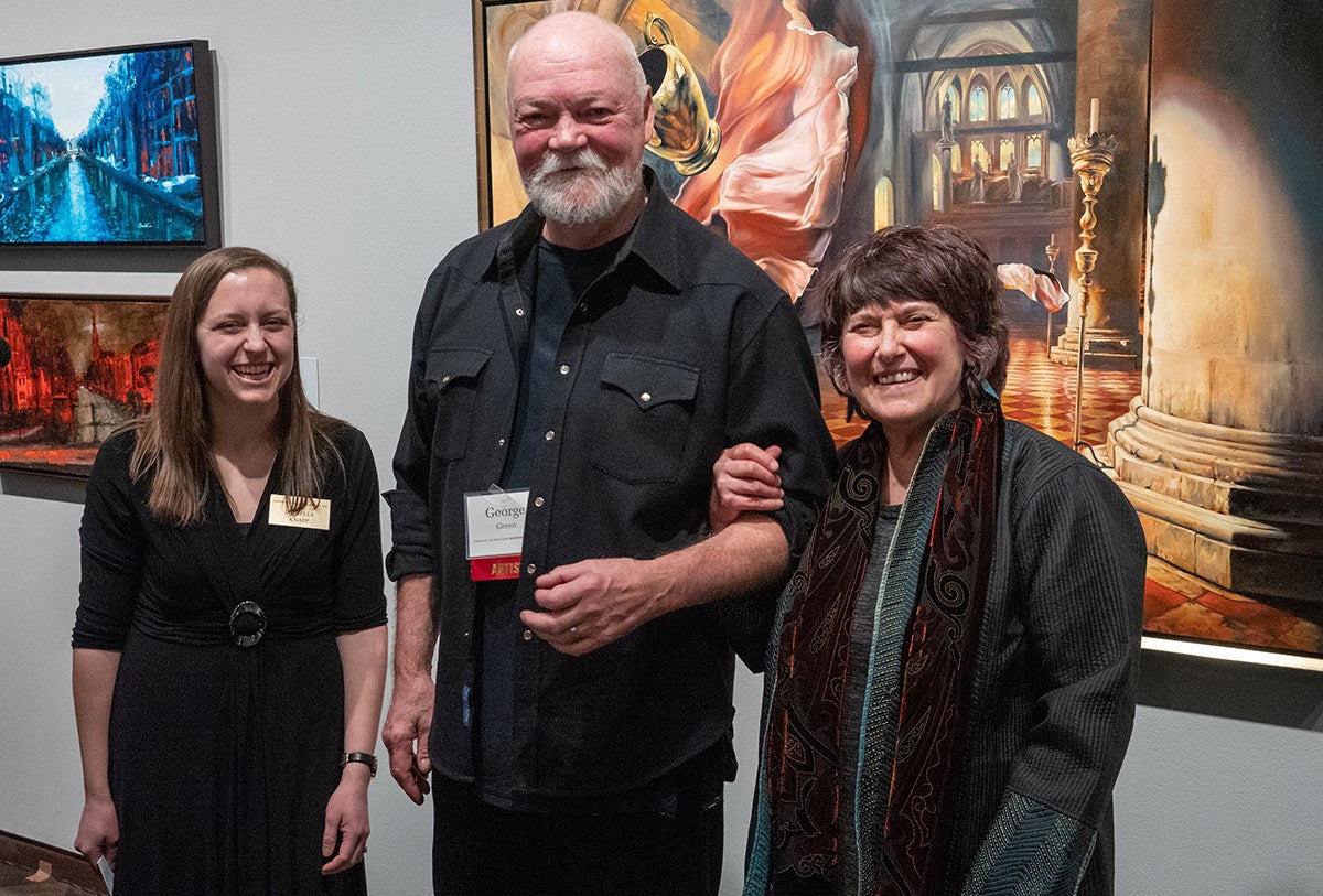Three people standing in front of a wall of paintings