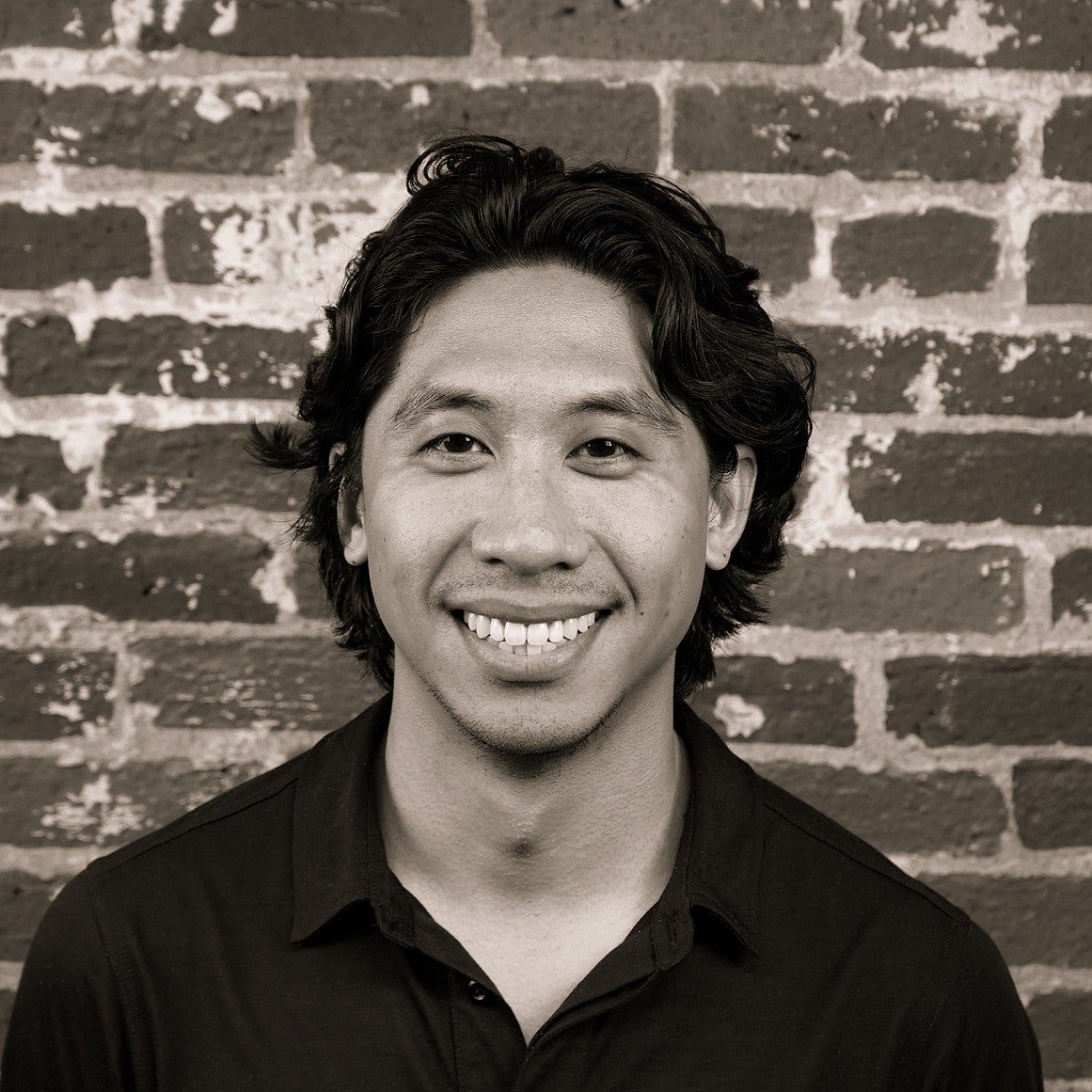 Photograph of a smiling SPD student, Aeryk Catipon, in front of a brick wall.