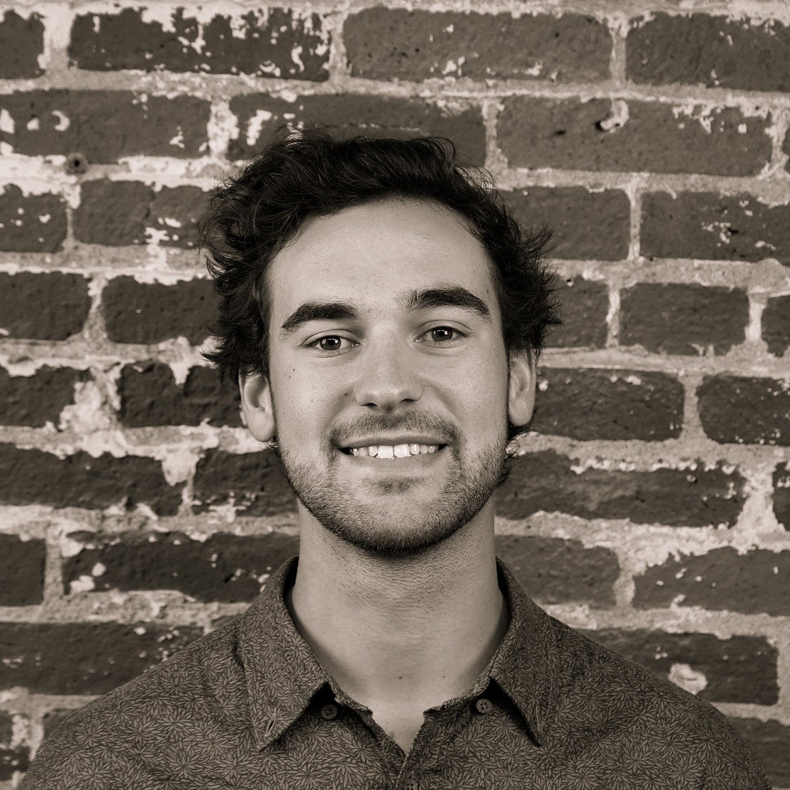 Photograph of a smiling first-year SPD student, Ryan Karow, in front of a brick wall.