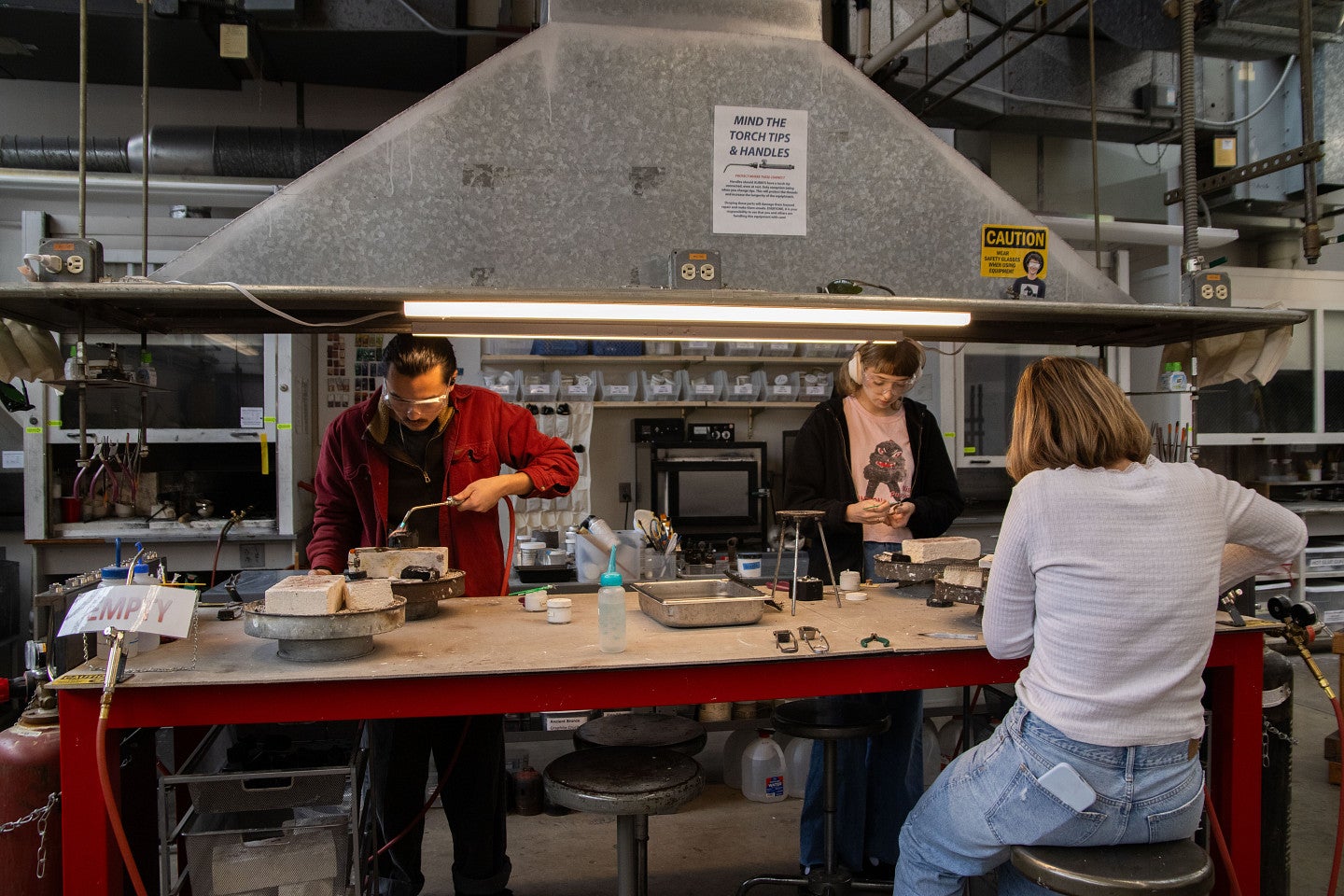 Students work on jewelry with torches in jewelry and metalsmithing studio. Decorative. 