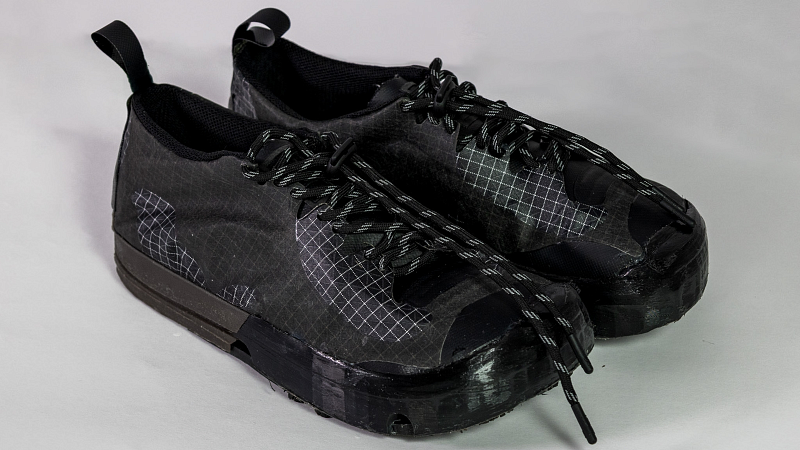 A pair of unbranded, black shoes with a flat sole and white, grid-like pattern throughout.