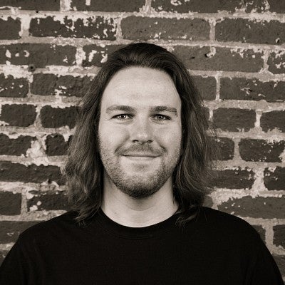Photograph of a smiling first-year SPD student, Joe Waits, in front of a brick wall.