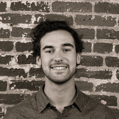 Photograph of a smiling first-year SPD student, Ryan Karow, in front of a brick wall.