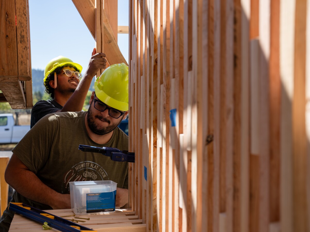 Two people in hard hats assemble a timber wall frame.