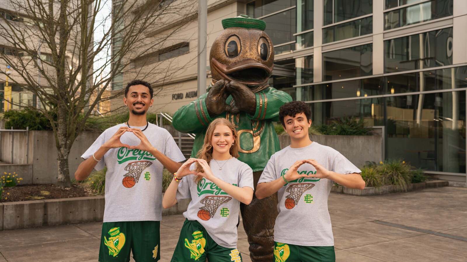 Three students pose with a Duck statue outdoors.