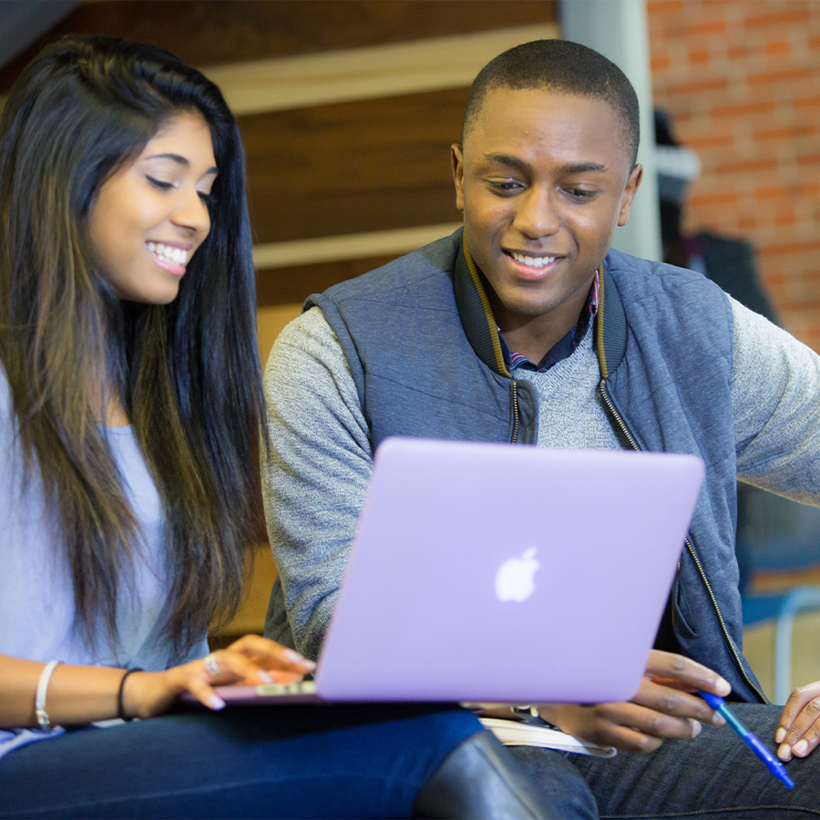 Two adult learners smile together over a laptop.
