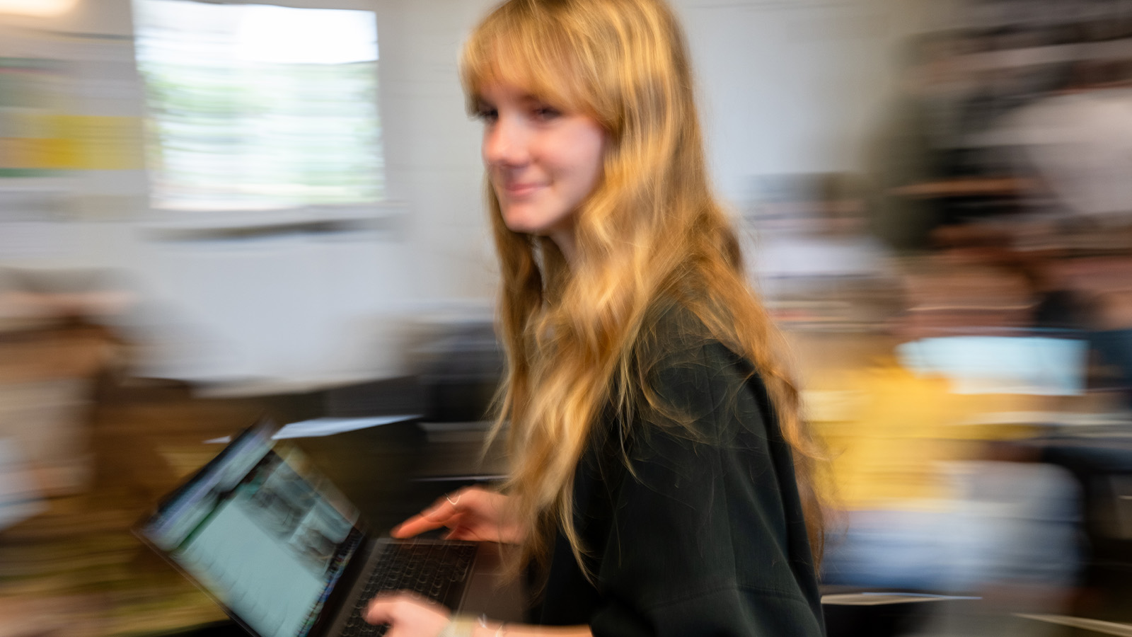 Student walking across a classroom holding laptop