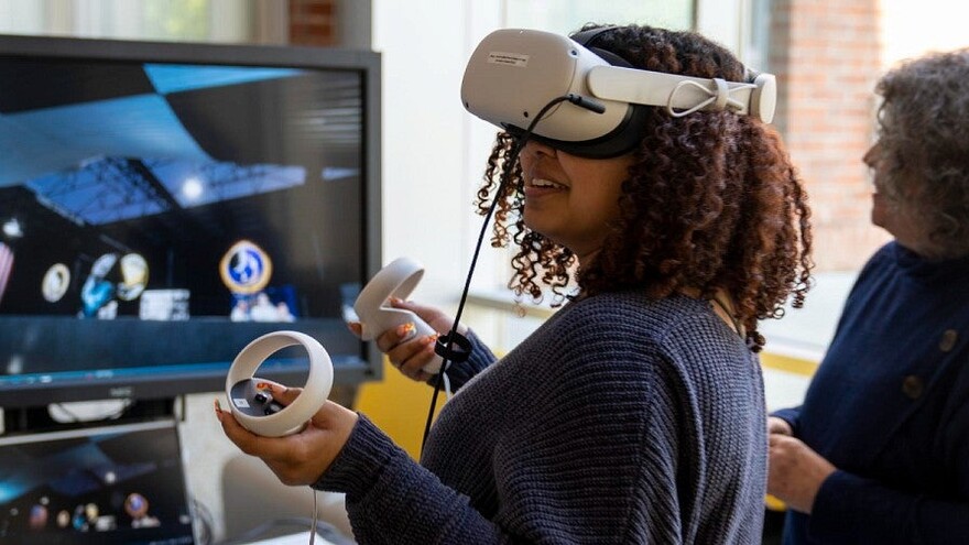 Classroom immersive media demonstration with a user wearing a VR headset and holding controllers.