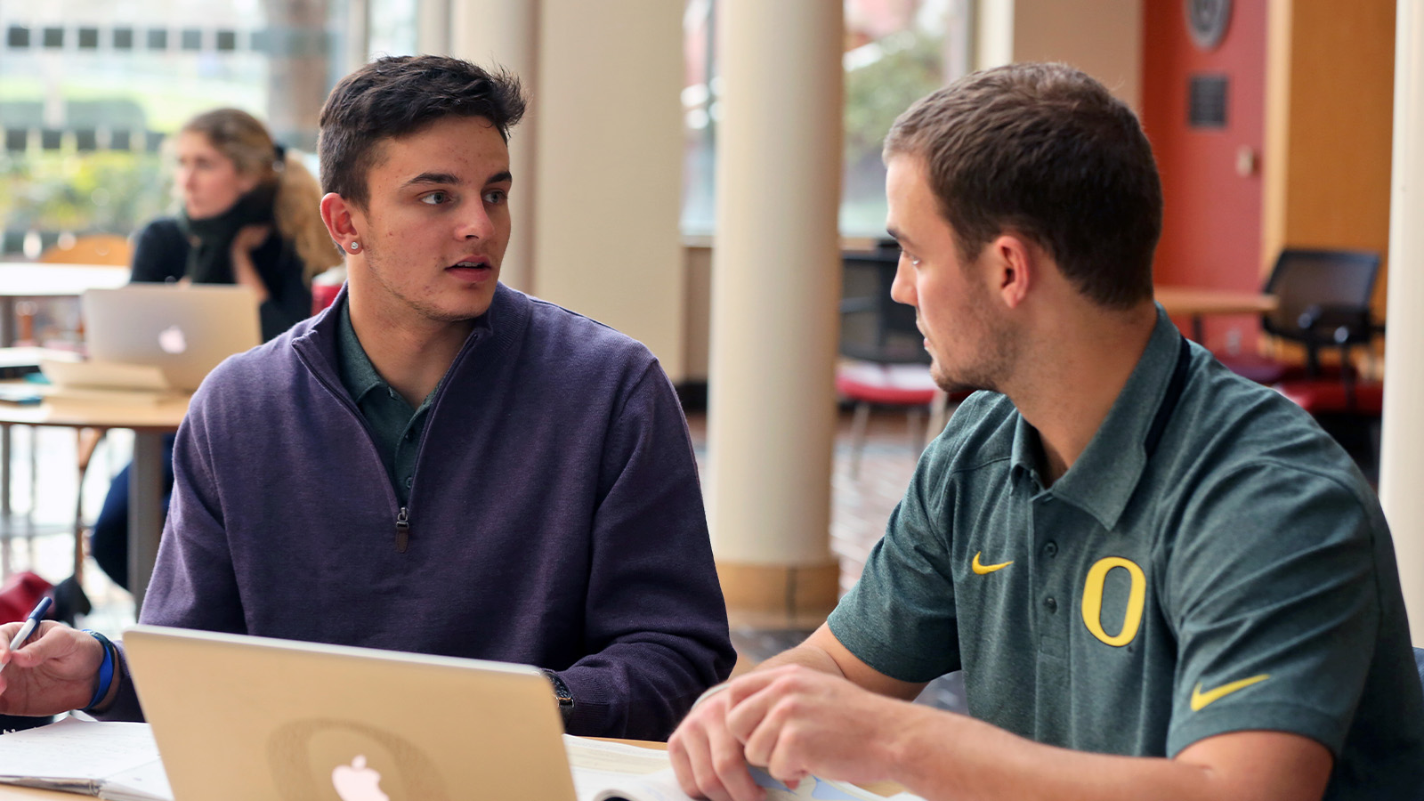 Two students collaborating while sitting at a table with a laptop