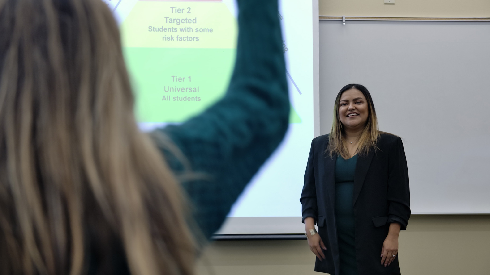 A presenter smiles as a student raises a hand.