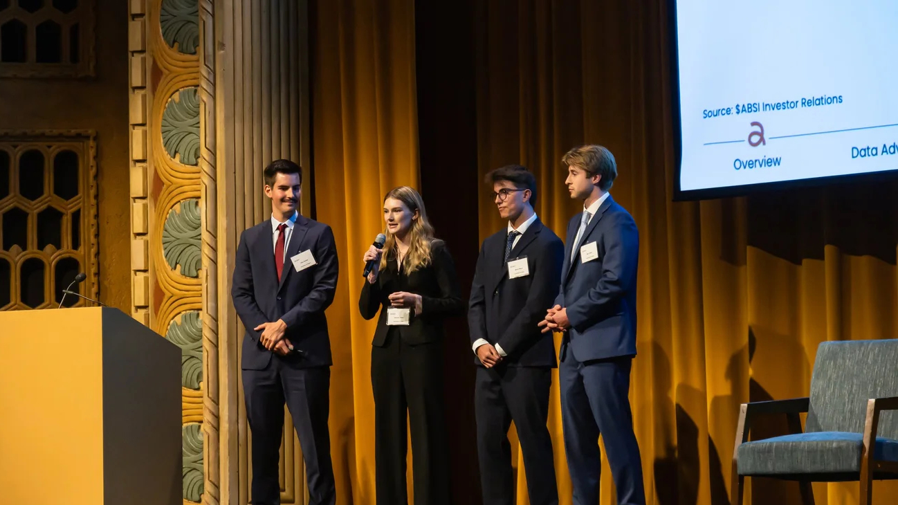 Four students standing on stage with one talking into a microphone