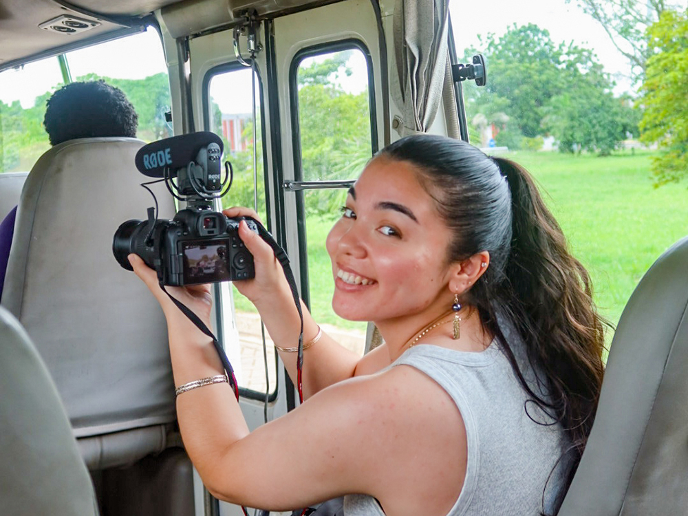 Student holding a camera while filming inside a bus