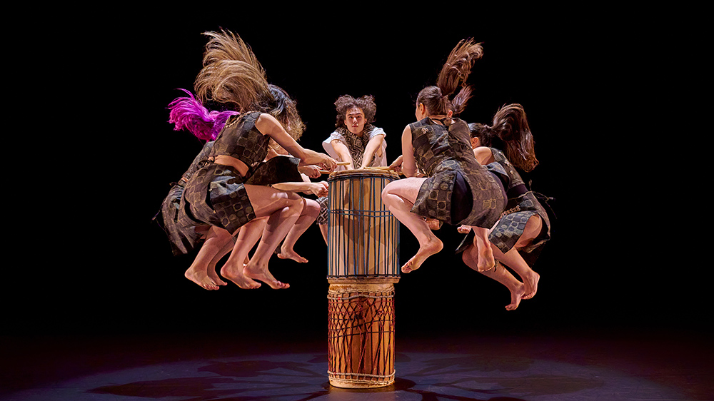 A group of dancers on stage dancing around a drum