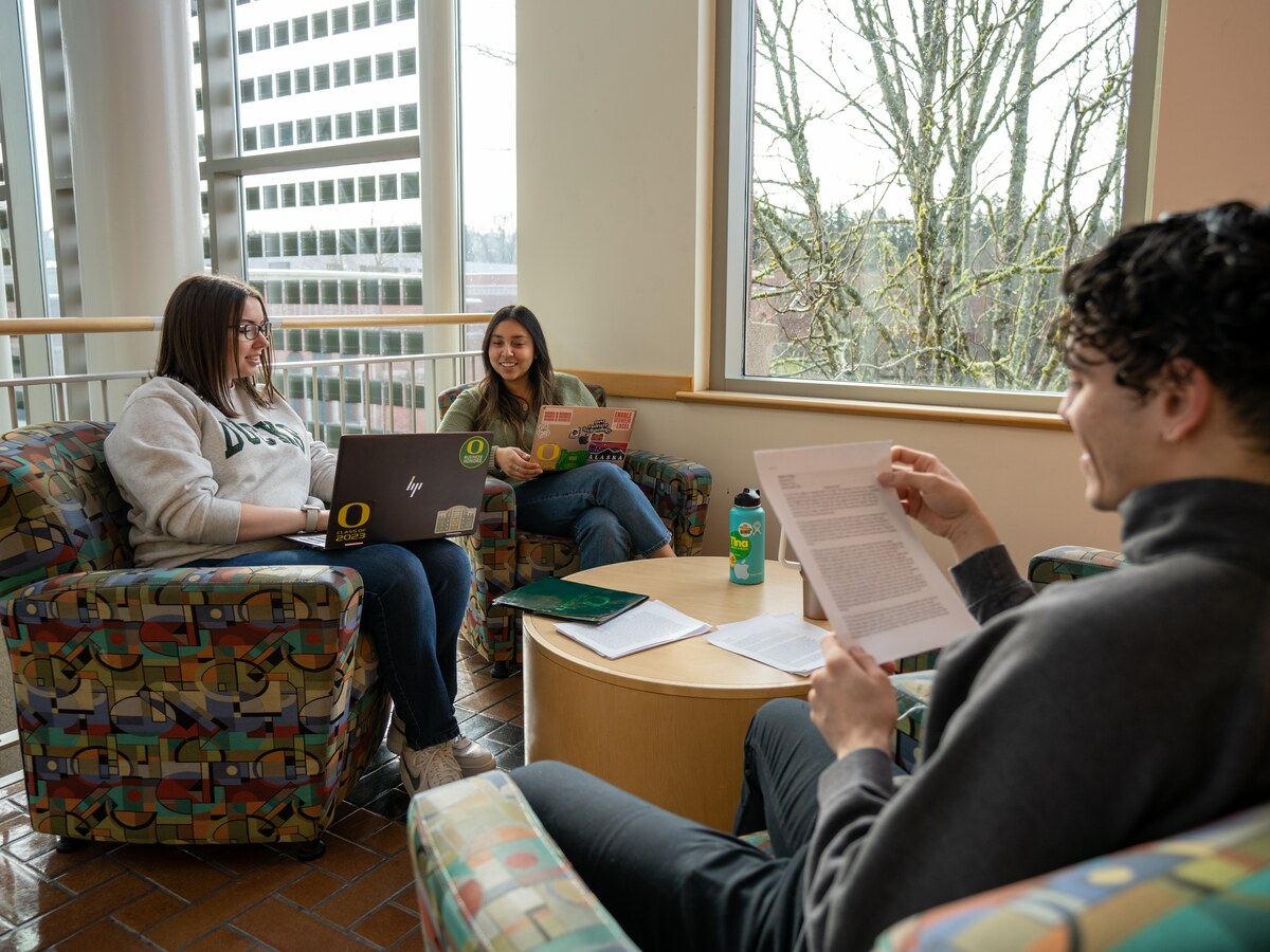Three students talk together around a table in a campus lounge.