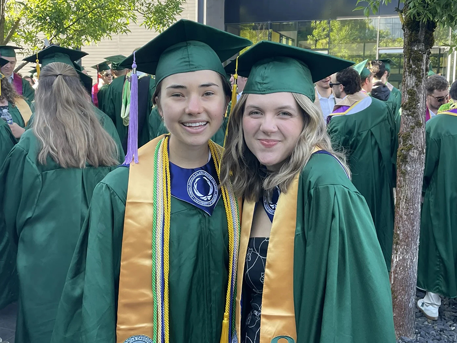 Two students smiling wearing graduation attire