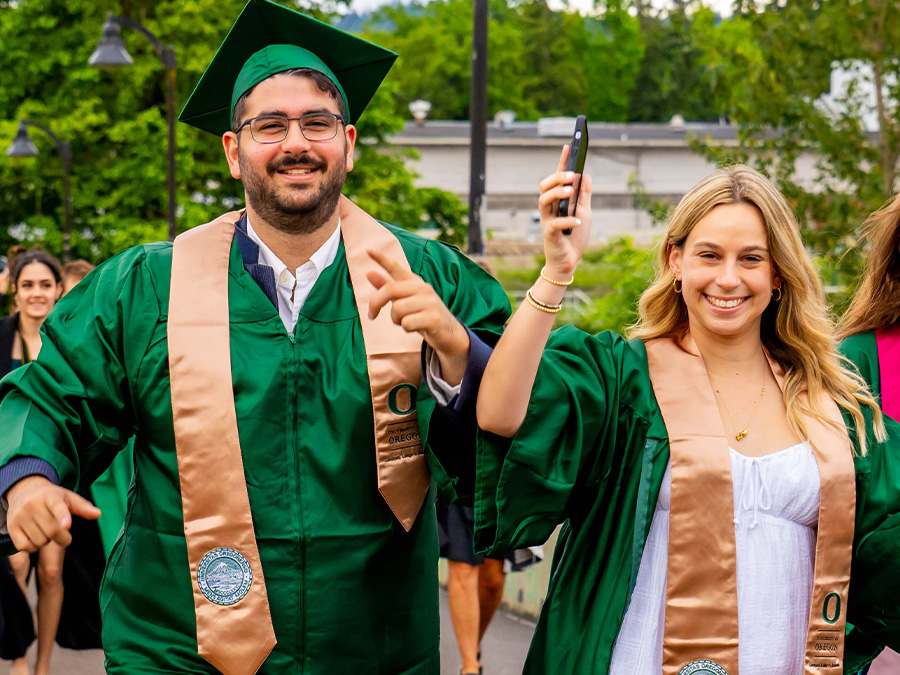 Two students in regalia crossing the Autzen bridge on their way to commencement