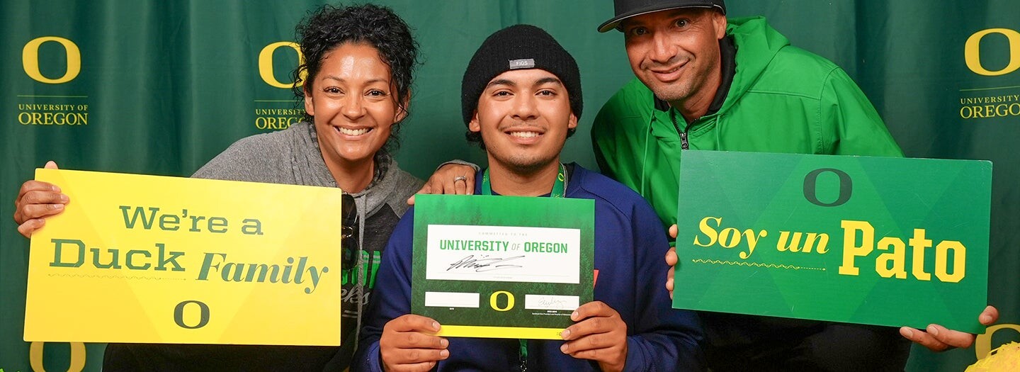 A family celebrates an Oregon admission with Duck Family and Soy un Pato signs.
