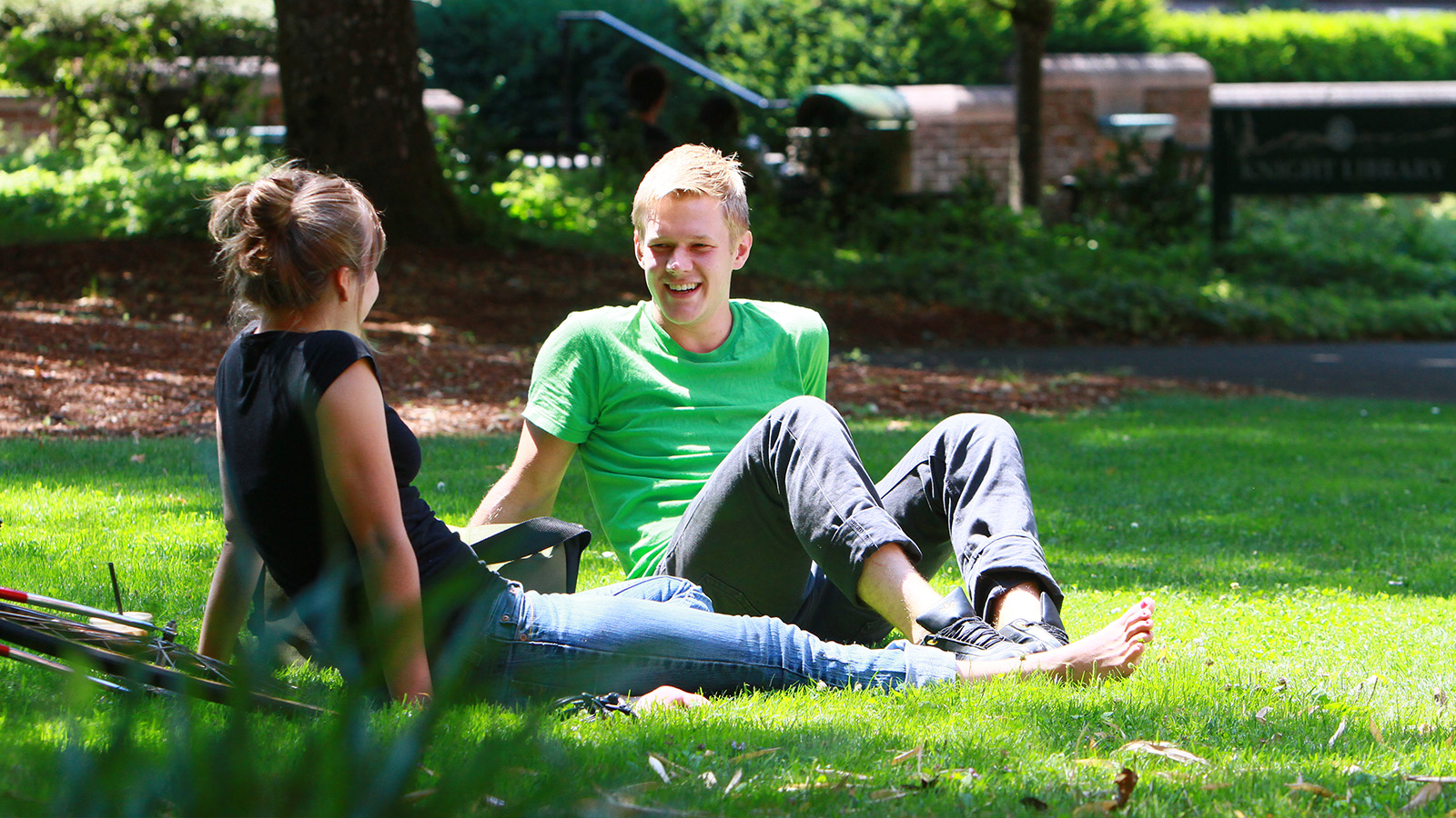 Two students sitting on a bright green campus lawn