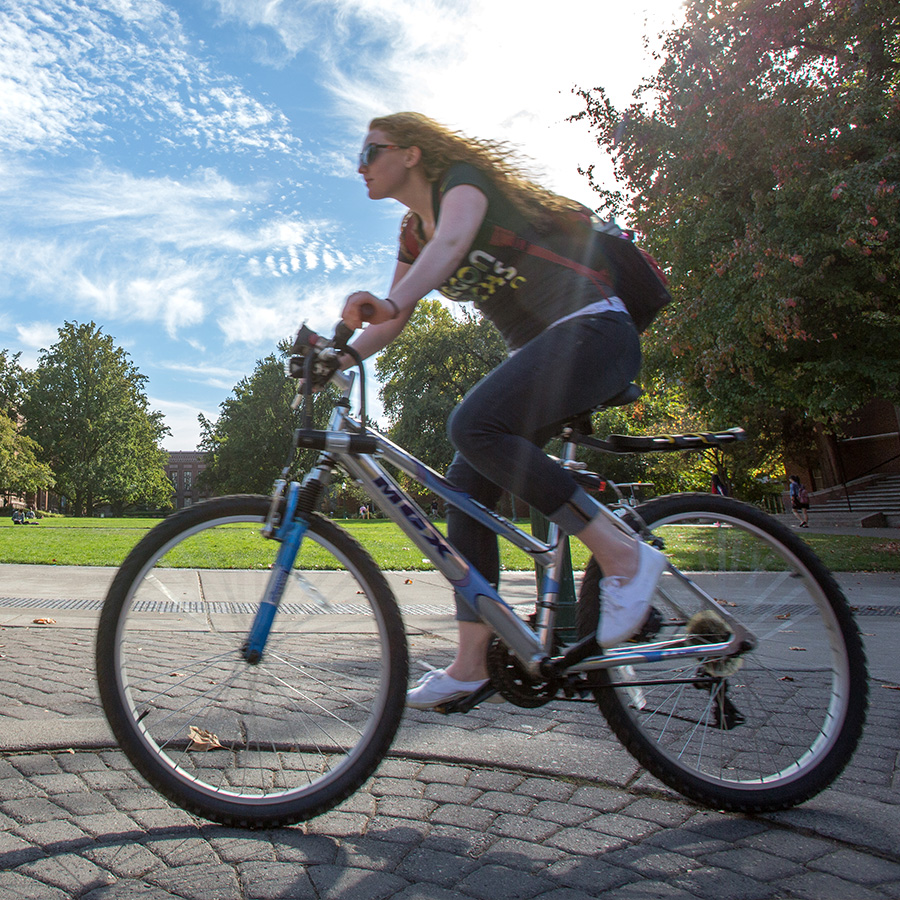 A young woman riding bike across campus on a sunny day