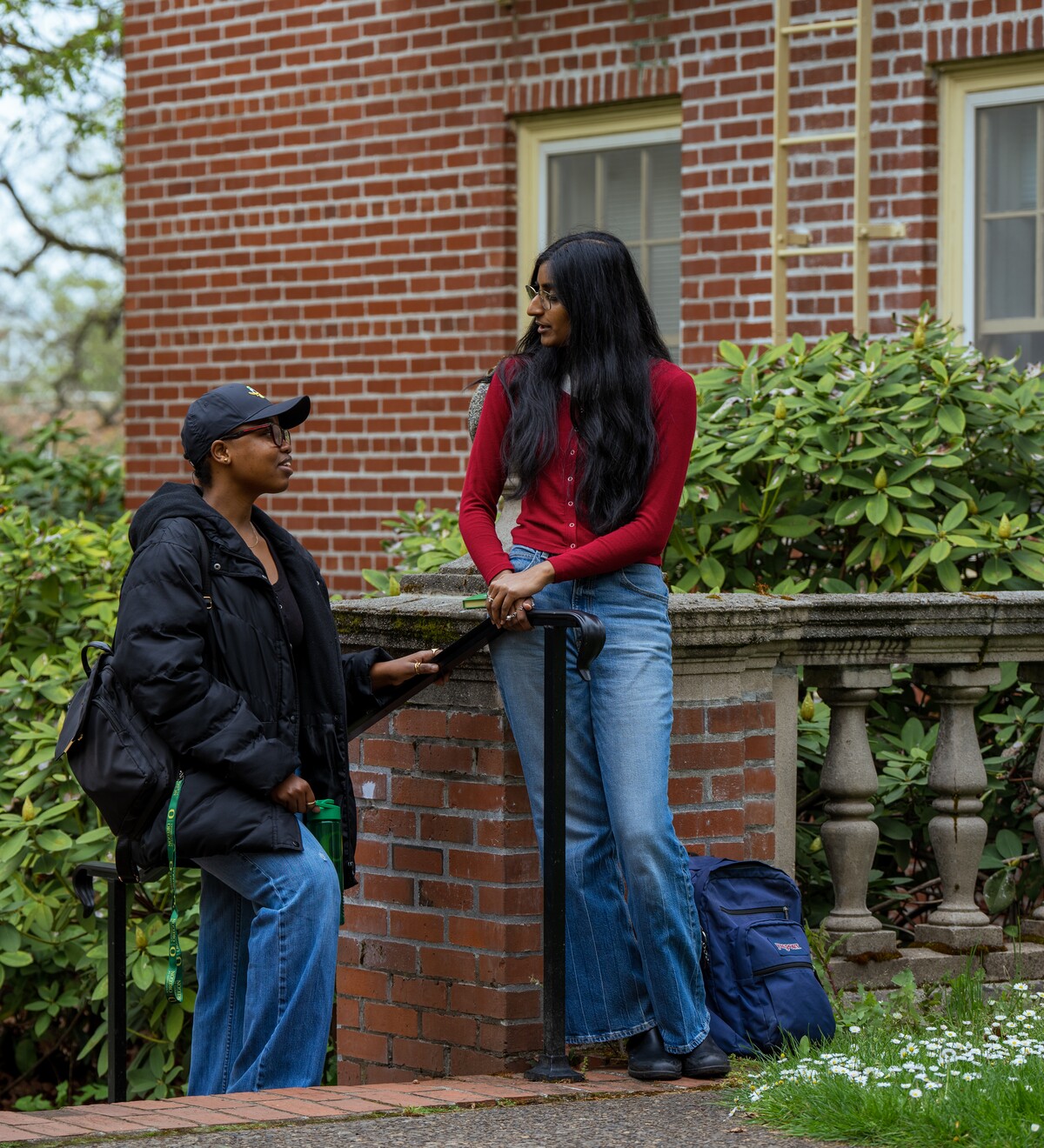 Two international students talk while standing in front of a brick building.
