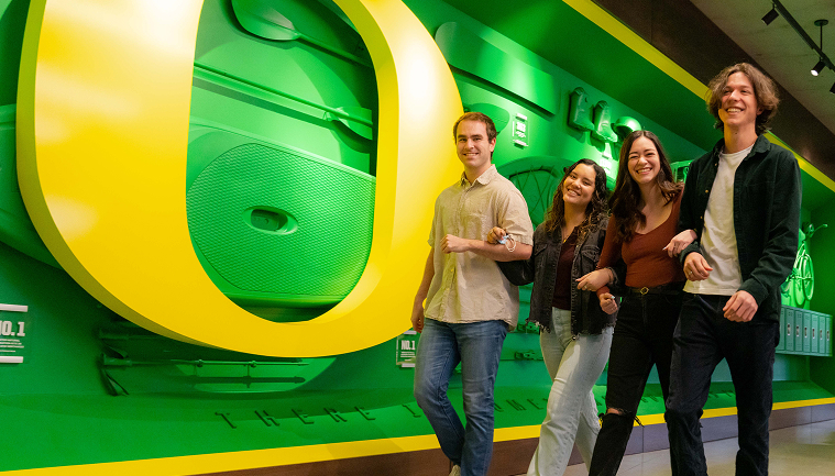 Four students walking in front of a big O on a wall