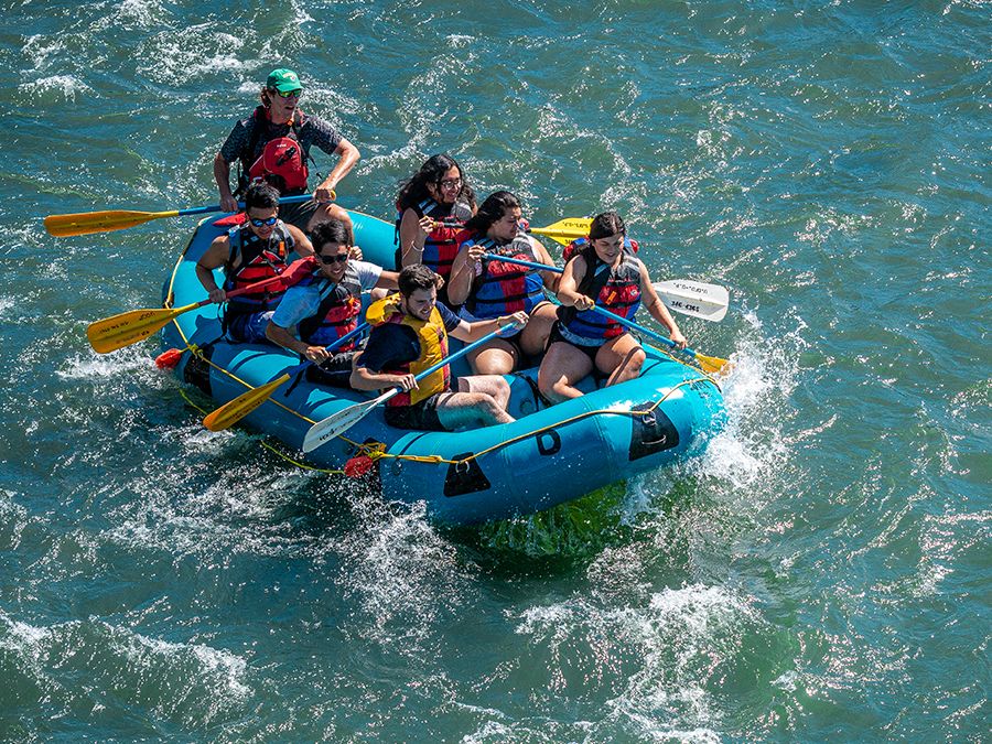 A group paddles a blue raft through churning whitewater.