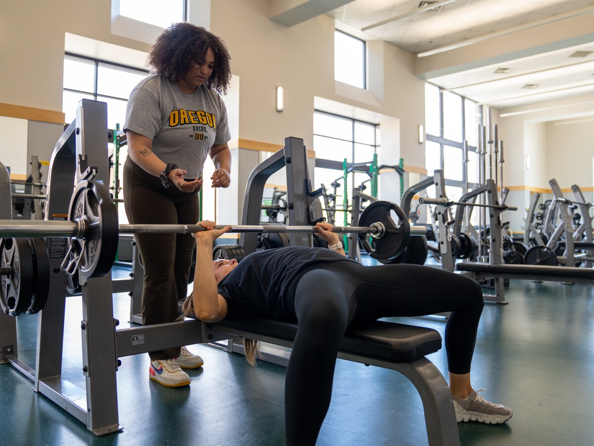 One person spots another during a bench press exercise in a UO fitness facility.