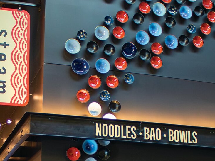 The Steam dining venue sign hangs above its counter advertising Noodles, Bao, and Bowls.