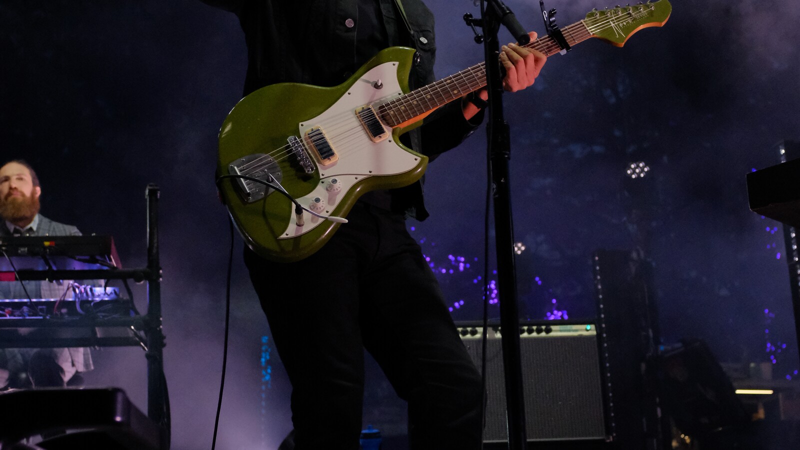 A guitarist performs beside a keyboardist under stage lights.