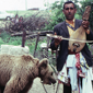 A man playing an instrument with a bear on a leash nearby