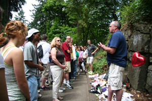 A group of people listen to a speaker near a memorial site