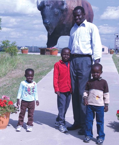A man and his three children standing near a giant buffalo statue