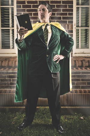 A professor wearing a cape and reading a book in a superhero pose