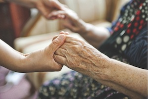 A young person holds hands with an elderly person
