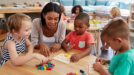 A teacher sits around a table with elementary school children  