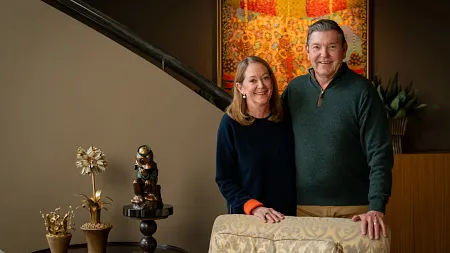 Ron and Chris Sauer smile together in their Portland home, standing in front of a vibrant abstract painting near a staircase.
