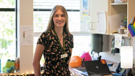 Anne Libby, a Ballmer Institute intern, smiles while standing at a clinic reception desk wearing a UO lanyard and name badge.