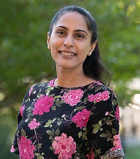 Portrait of a smiling woman with long dark hair tied back wearing a floral blouse