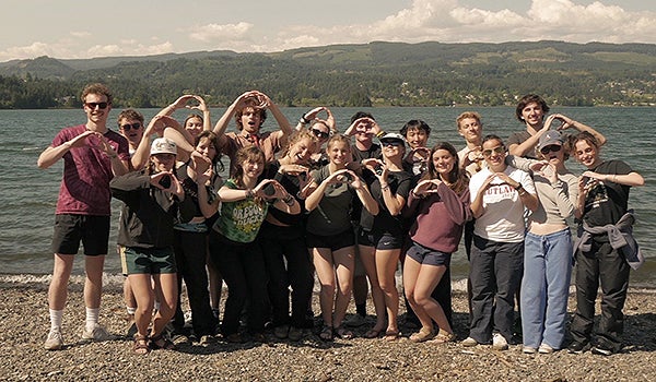 Large group of students stand along the shore of a lake