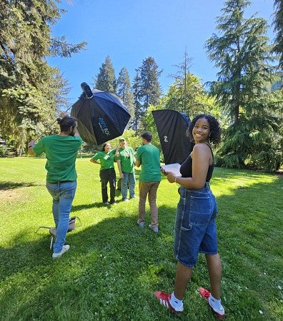 Student helping with a photo shoot outside among the trees