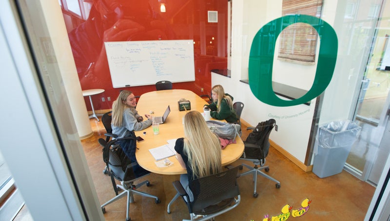 Photo of conference room with students meeting. Green O on the window outside.