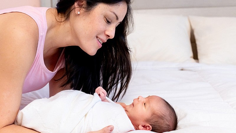 person looking down on an infant laying on a bed