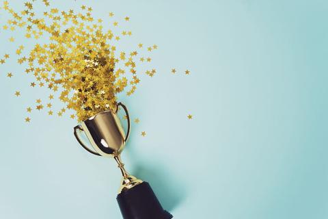 Gold star confetti spilling out of a gold trophy on a light blue background.