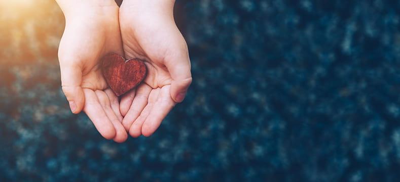 Hands holding a wooden red heart.