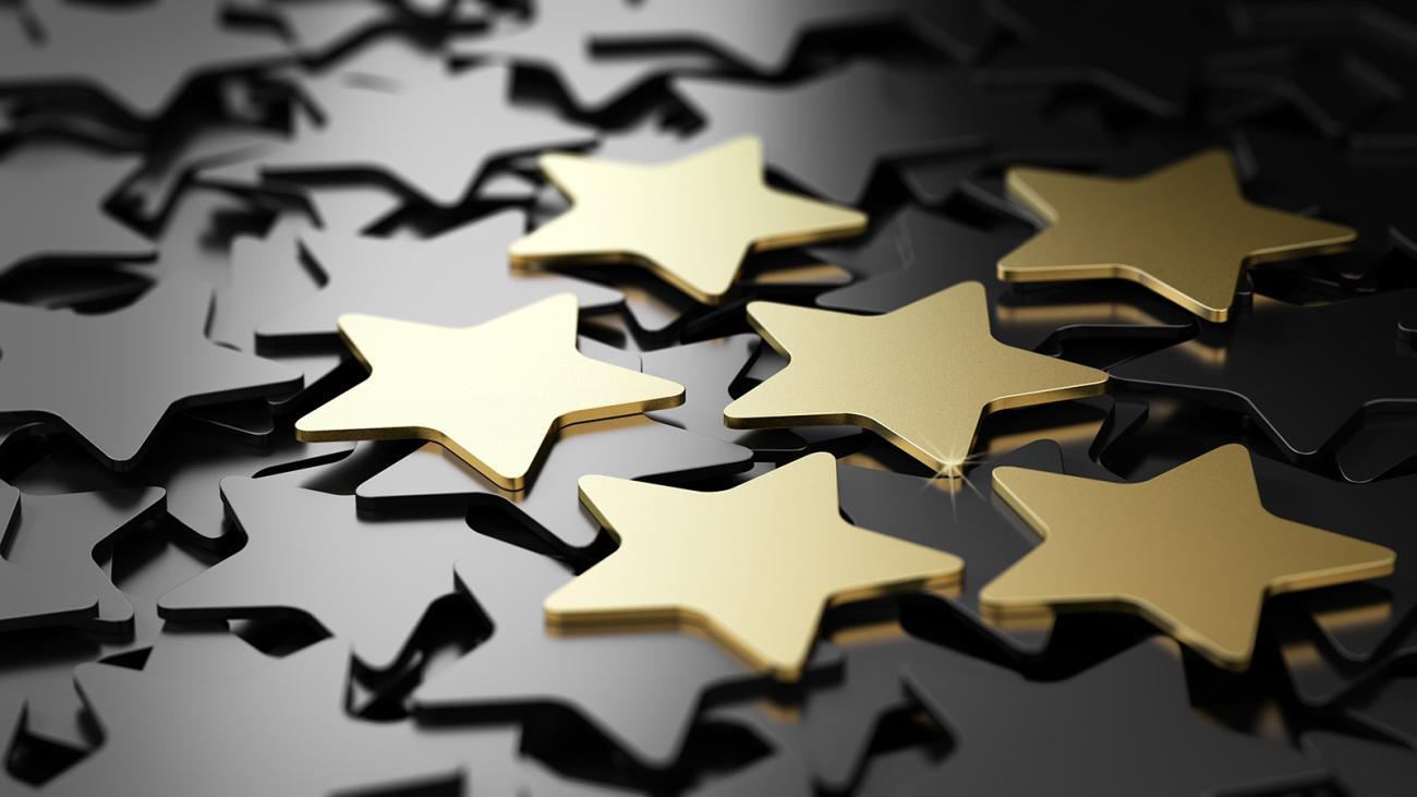 A stock image of metalic stars laid out, with 5 prominent gold ones resting on top.
