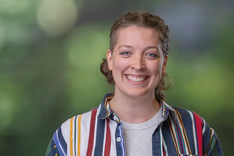 Smiling woman with hair in braids wearing a shirt with multicolored vertical stripes