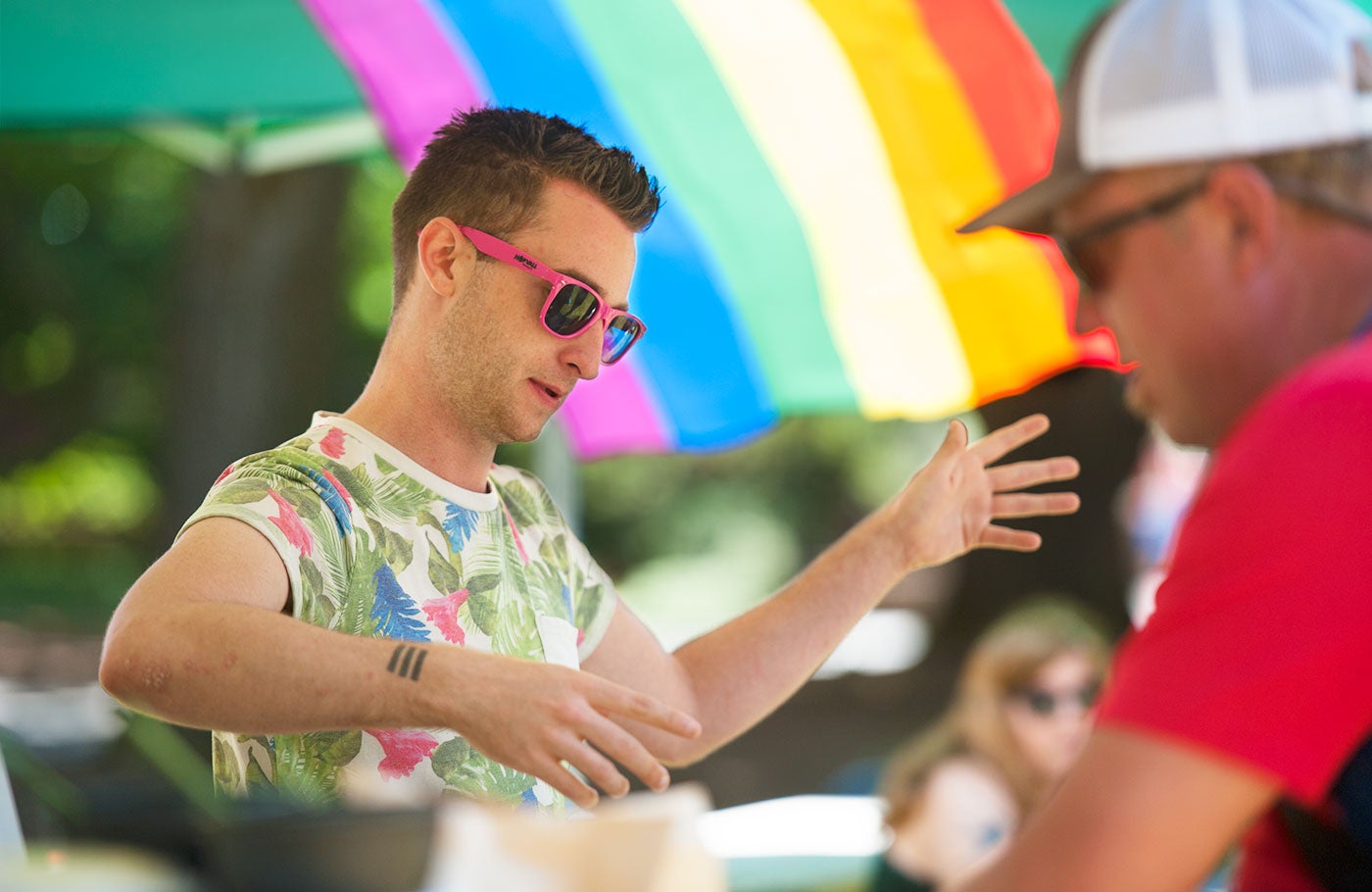 Two students connect at the LGBTQ picnic with a rainbow flag in the background.