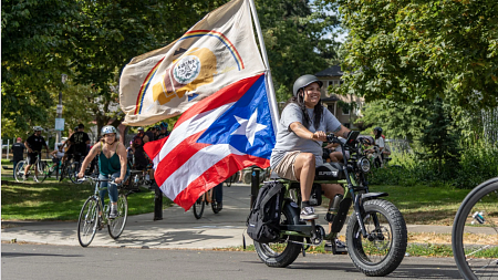 Alexis Vasquez, who uses they/them pronouns and identifies as Taino, proudly displays the Navajo Nation and Puerto Rico flags as they lead the cyclists to the next stop during the ride. 